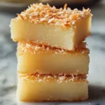 Stacked butter mochi hawaii squares topped with toasted coconut on marble