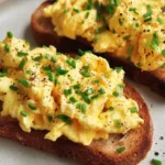 Plate of scrambled egg toast topped with herbs and spices