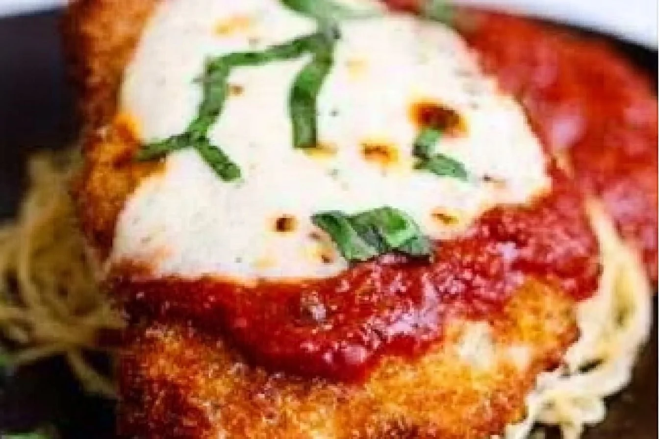 Easy baked chicken parmesan served with pasta and fresh herbs