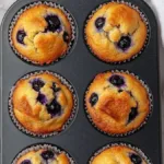 Hearty blueberry protein muffins fresh out of the oven with blueberries visible.
